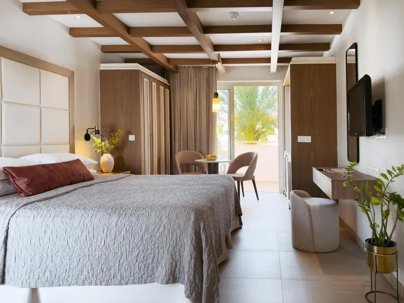 Chambre lumineuse avec un grand lit et un espace repas près d'une baie vitrée.