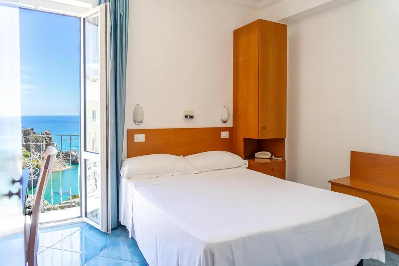 Chambre lumineuse avec vue sur la mer depuis un balcon.