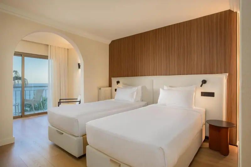 Une chambre lumineuse avec deux lits simples et un accès à un balcon.