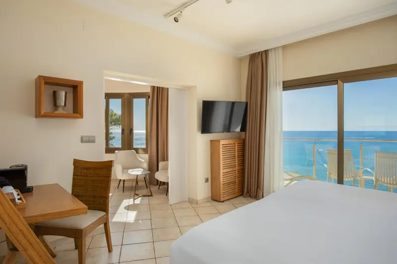 Une chambre lumineuse avec un lit et un bureau donnant sur une vue mer.