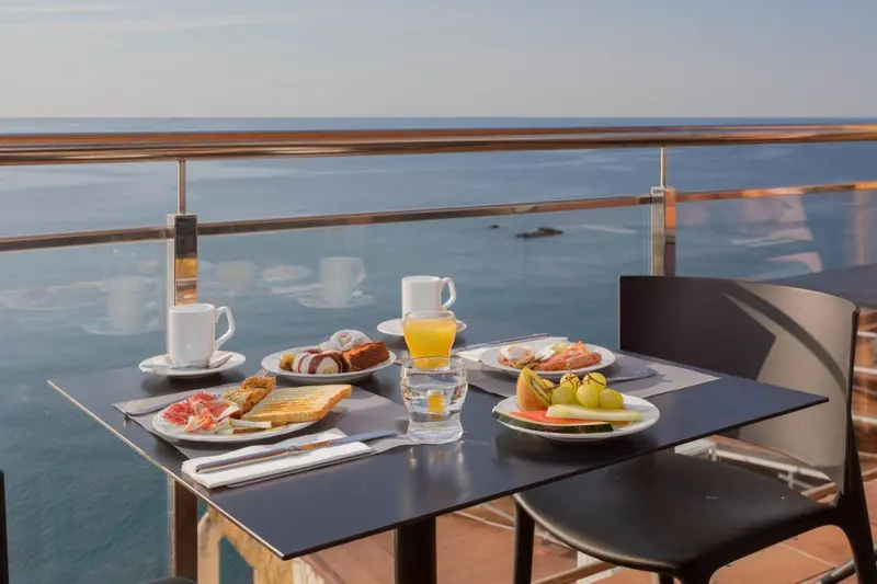 Une table est dressée pour le petit-déjeuner sur une terrasse avec vue sur la mer.