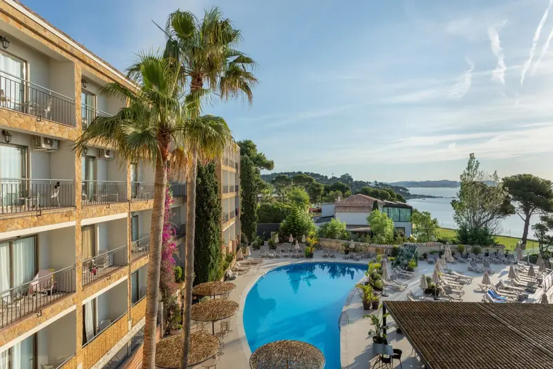 Vue aérienne d'un bâtiment beige avec des balcons donnant sur une piscine et la mer.