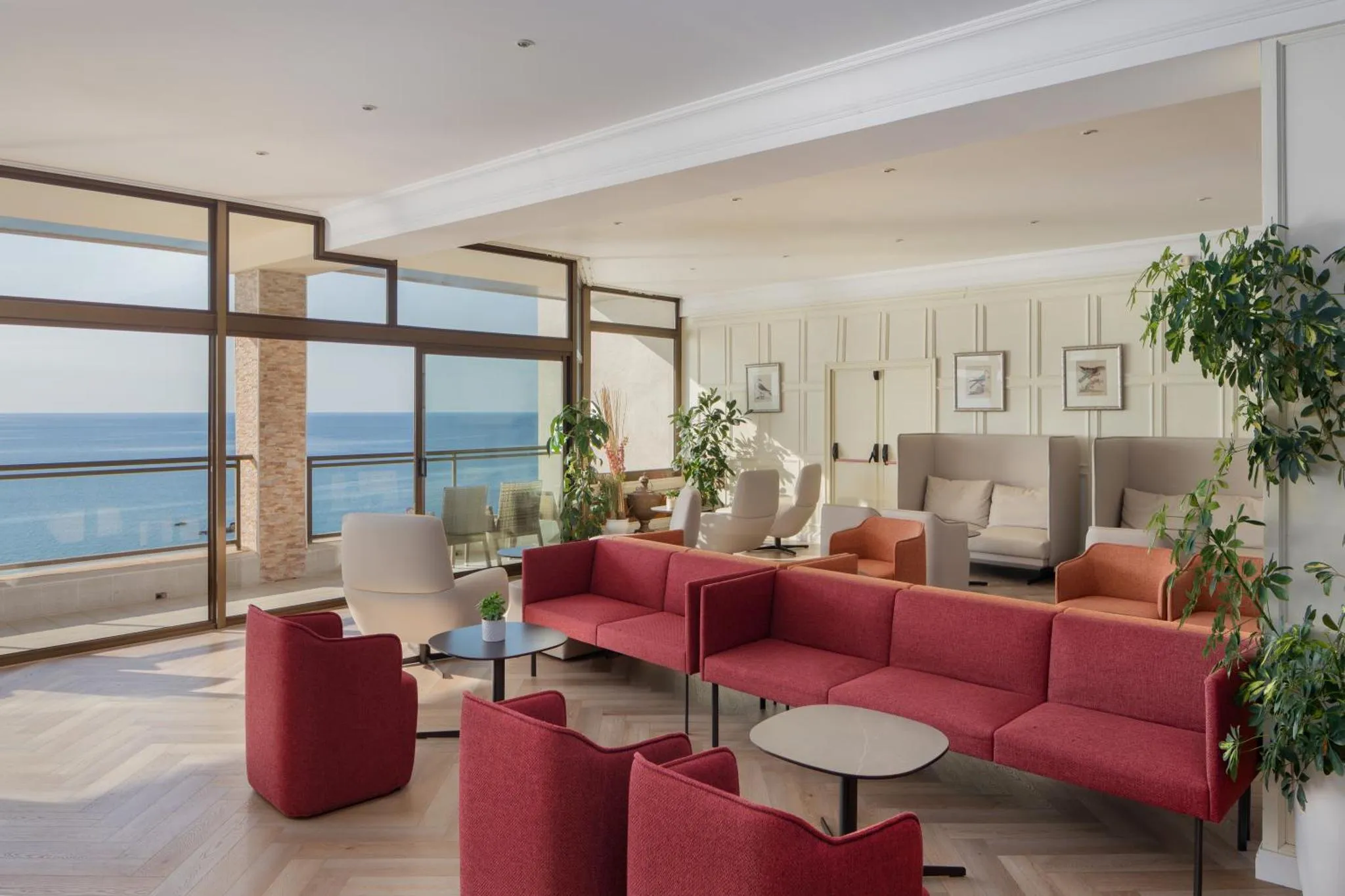 Un espace de détente intérieur avec des canapés et des fauteuils face à une grande baie vitrée donnant sur la mer.