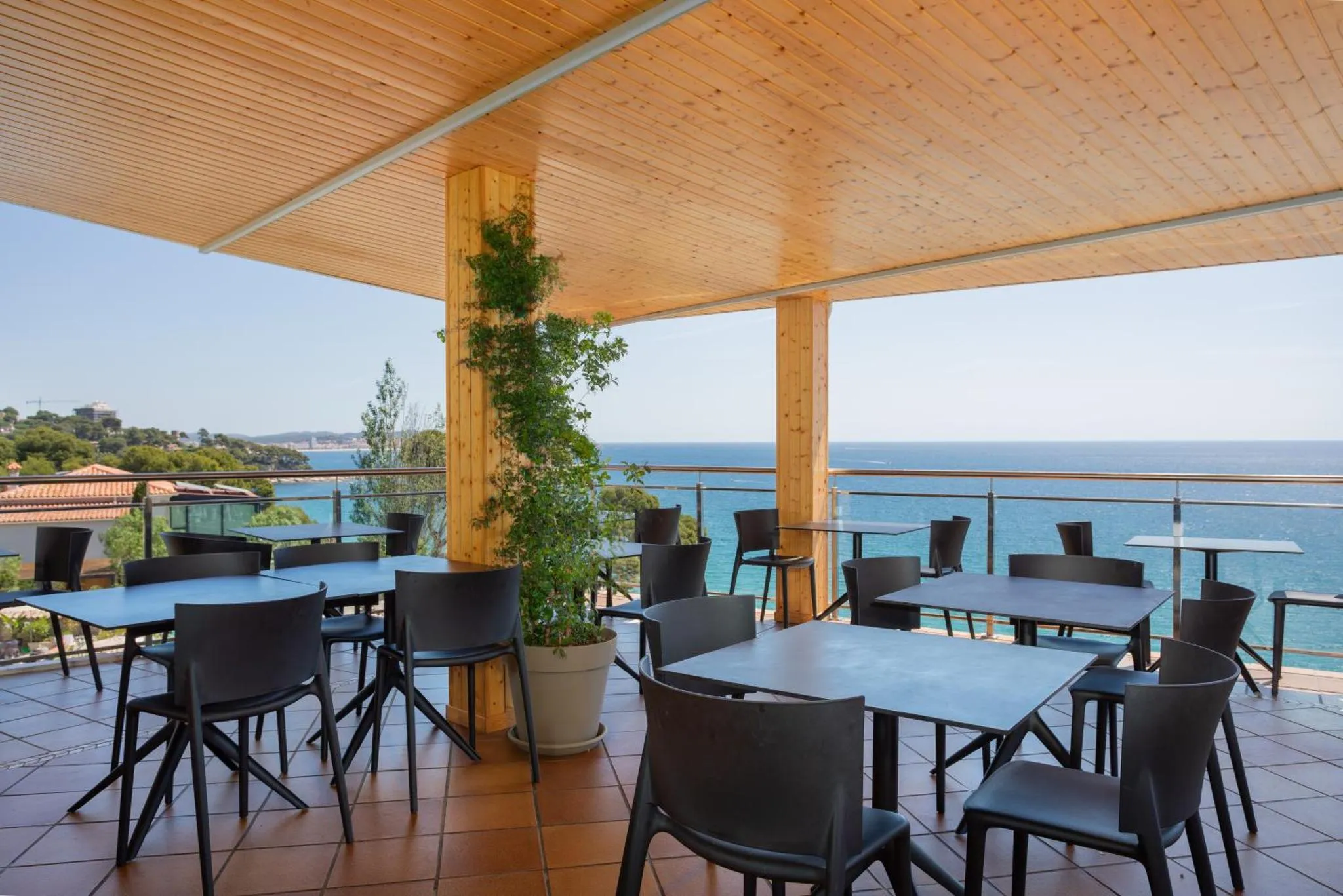 Terrasse ombragée avec tables et chaises donnant sur la mer.