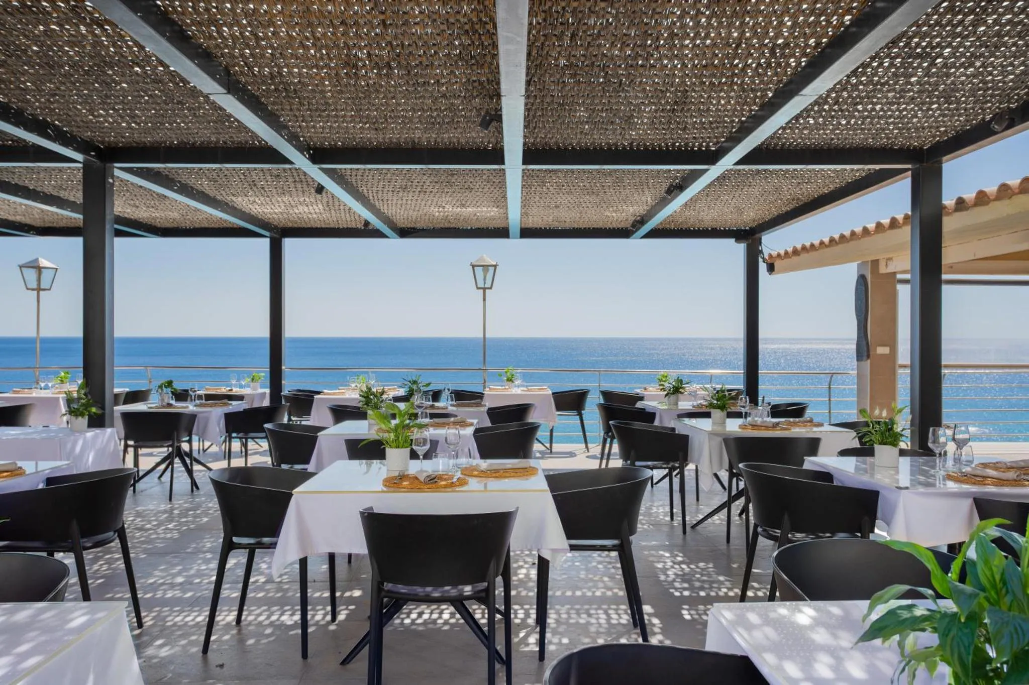 Une terrasse ombragée avec des tables dressées face à la mer.