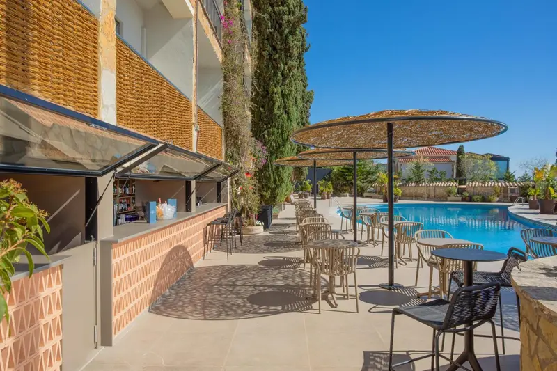 Terrasse avec bar et tables près d'une piscine ensoleillée.