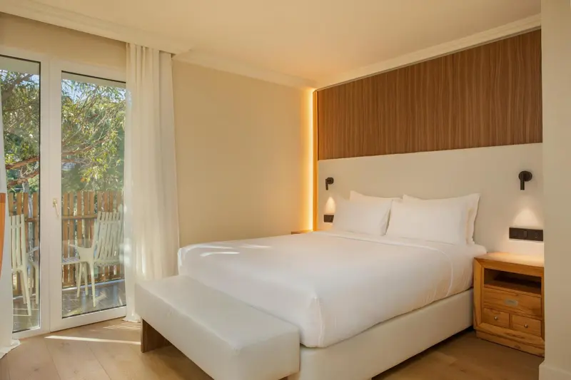 Chambre lumineuse avec un grand lit et une baie vitrée donnant sur une terrasse.
