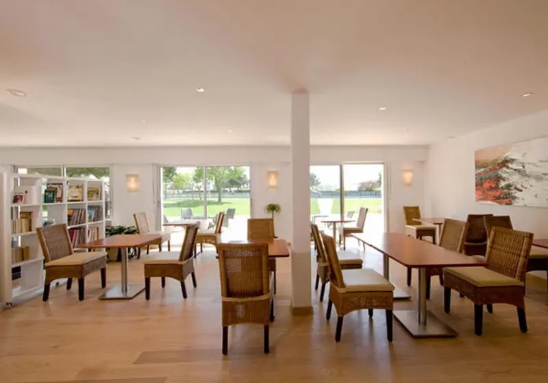 Une salle lumineuse avec des tables et des chaises près de grandes baies vitrées.
