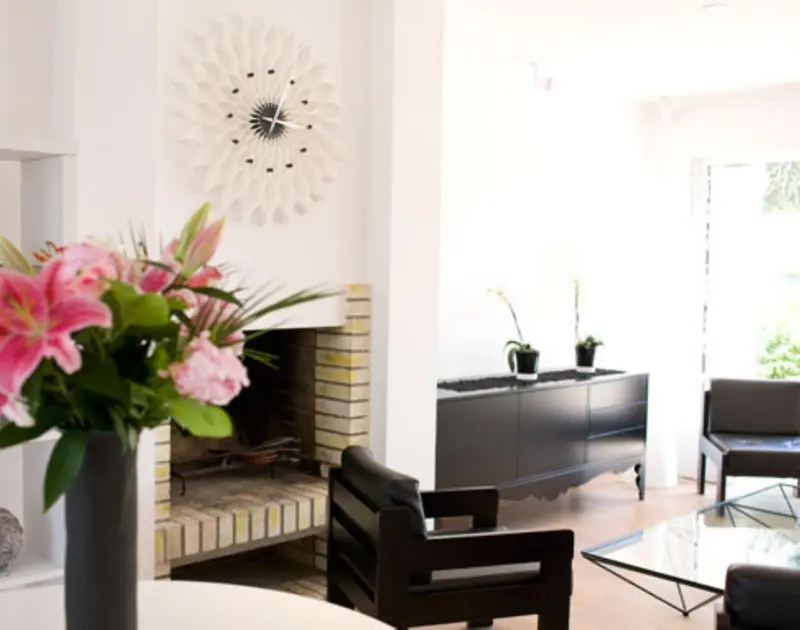 Un salon clair avec une cheminée et des fleurs roses.