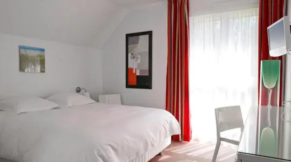 Une chambre lumineuse avec un lit blanc et des rideaux rouges.