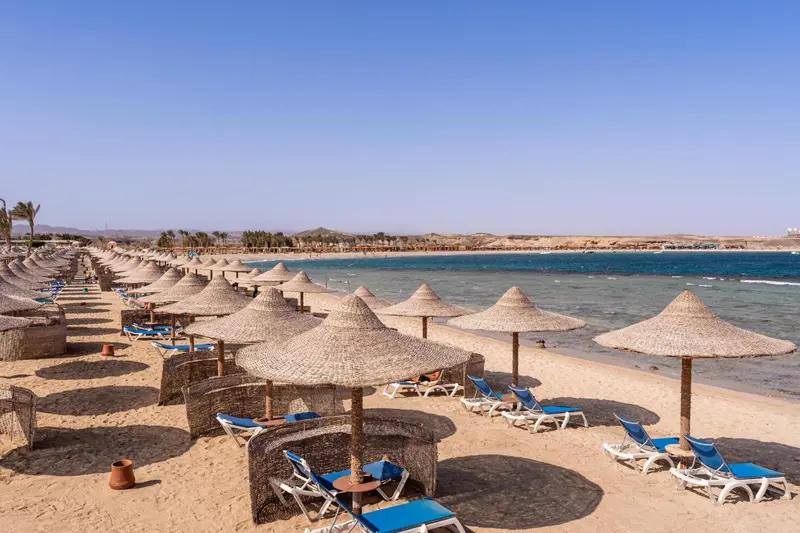 Plage de sable avec parasols en chaume et transats bleus.