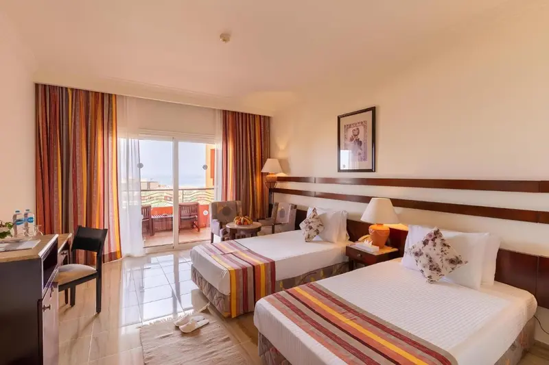 Chambre lumineuse avec deux lits et balcon donnant sur la mer.