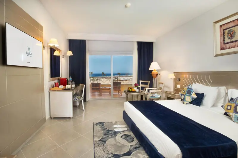 Chambre lumineuse avec un grand lit et une vue sur la mer par une baie vitrée.