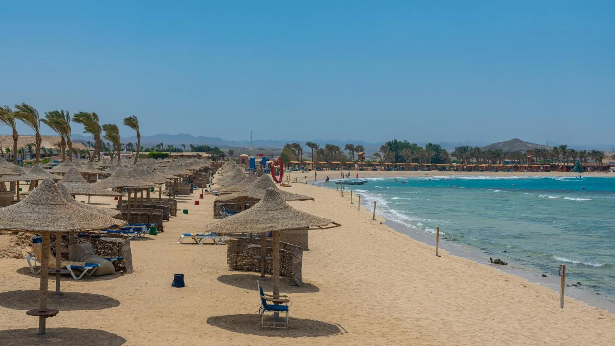 Plage de sable fin avec parasols et transats en bord de mer.