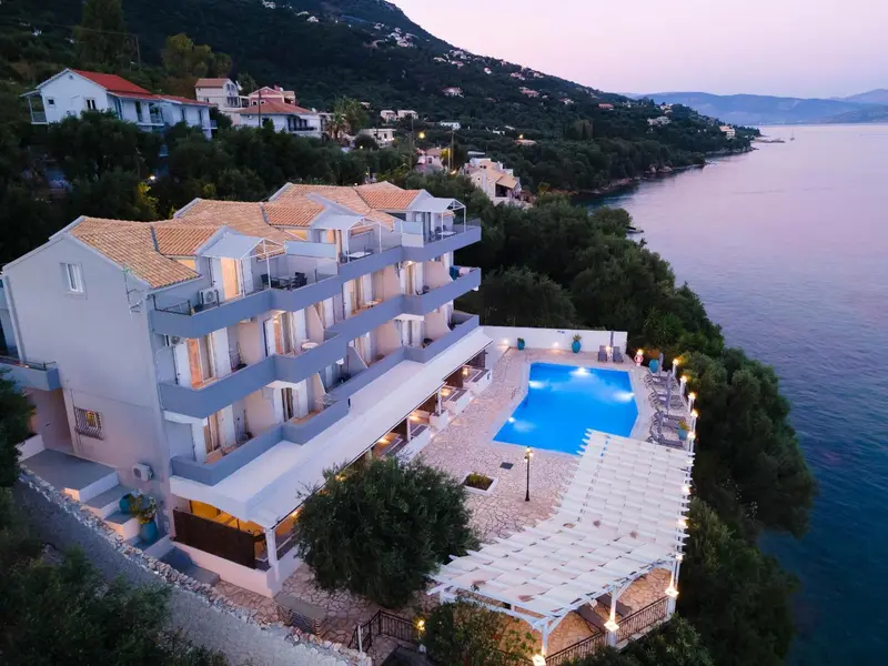 Vue aérienne d'un bâtiment blanc avec piscine et végétation luxuriante au bord de la mer.