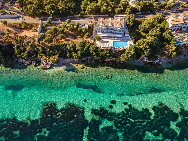 Vue aérienne d'un bâtiment blanc au bord de l'eau turquoise et rocheuse.