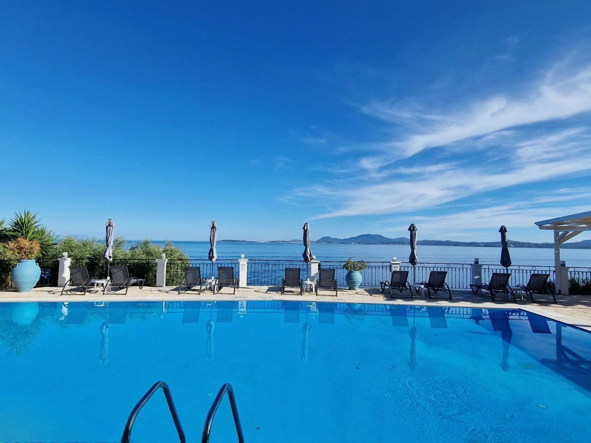 Piscine bleue avec transats et vue sur la mer.