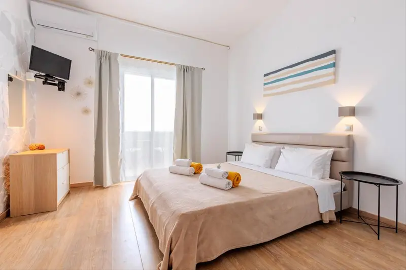Chambre lumineuse avec un grand lit et un accès à une terrasse.