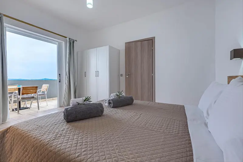Chambre lumineuse avec un grand lit et un accès à une terrasse.