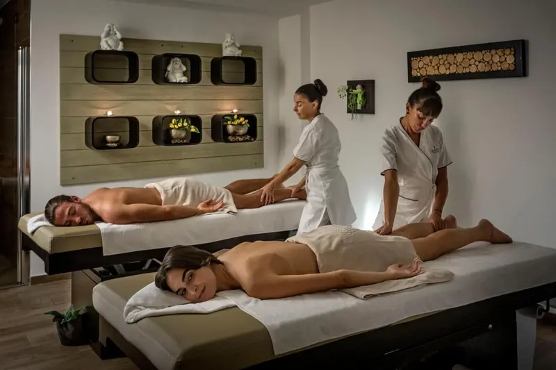 Deux personnes allongées sur des tables de massage reçoivent un soin dans une salle lumineuse.