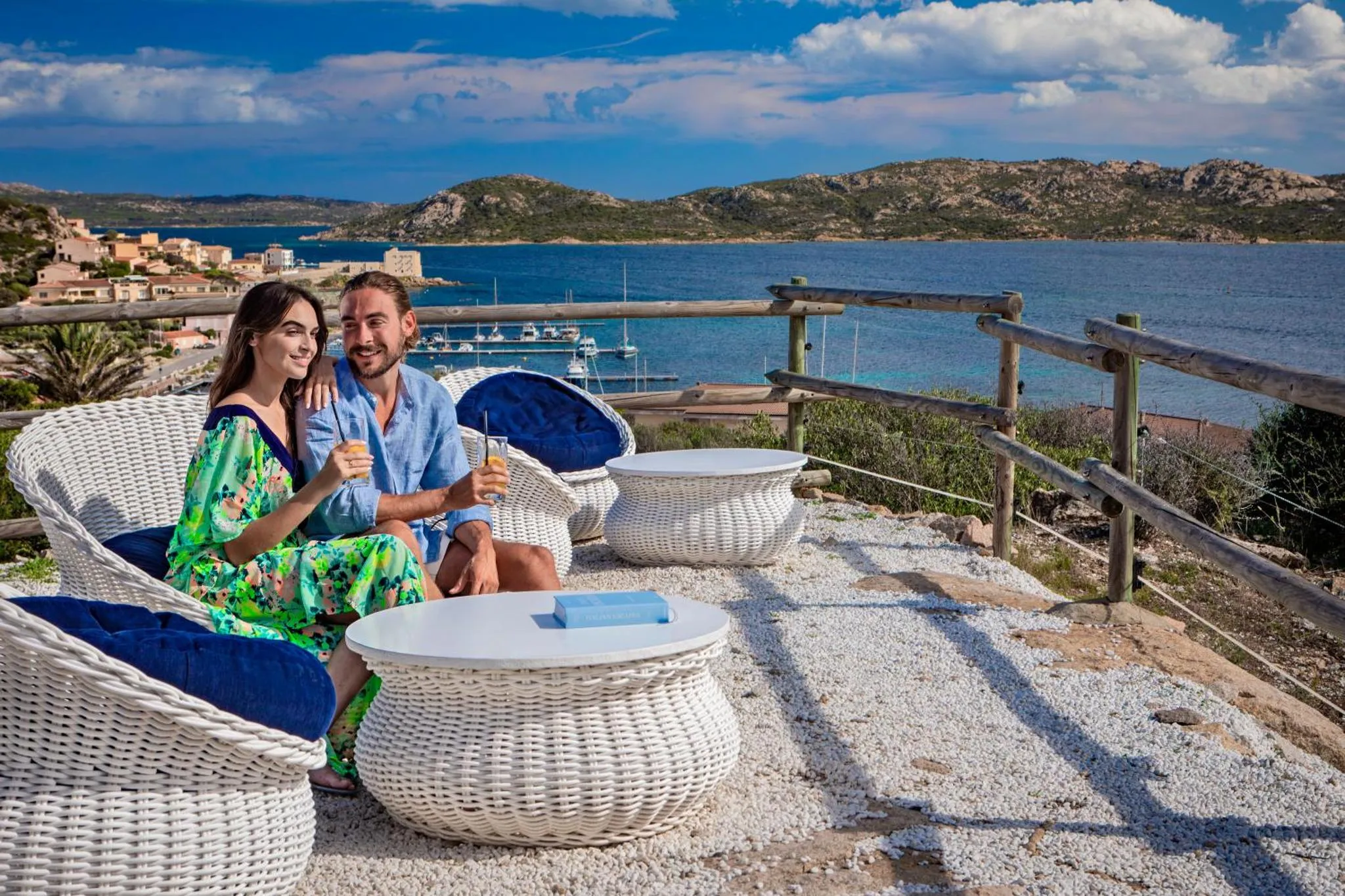 Un couple se détend sur une terrasse avec vue sur la mer et un port de plaisance.