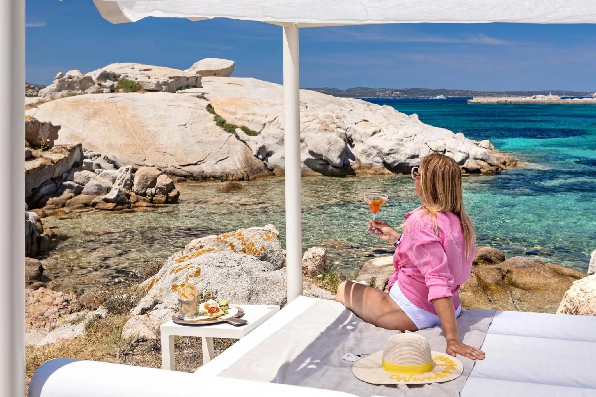 Une femme déguste une boisson et un repas face à la mer.