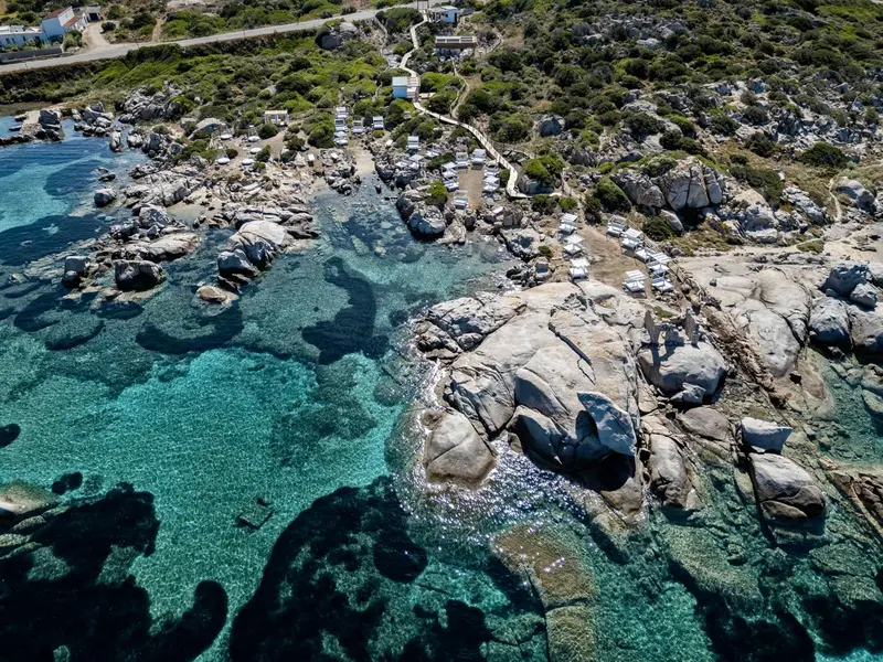 Vue aérienne d'une crique rocheuse avec des parasols et des transats sur une plage.