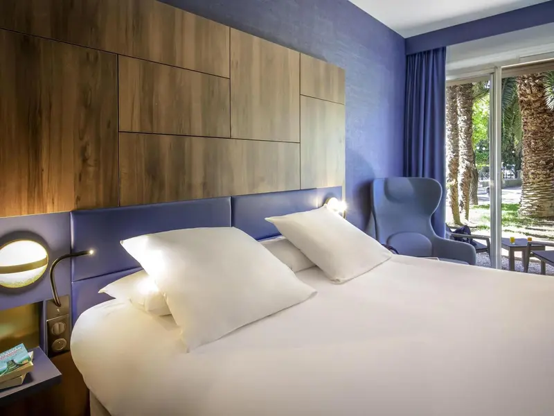 Une chambre lumineuse avec un grand lit et un fauteuil bleu.