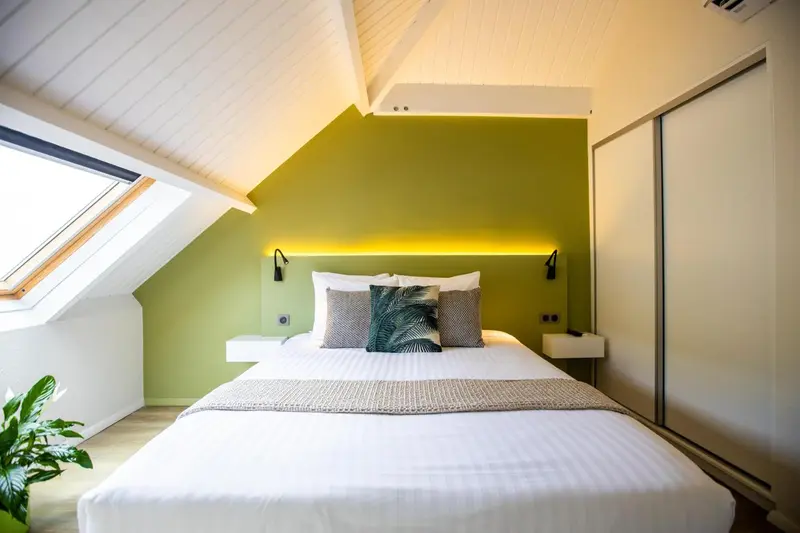 Une chambre lumineuse avec un lit double et un mur vert.