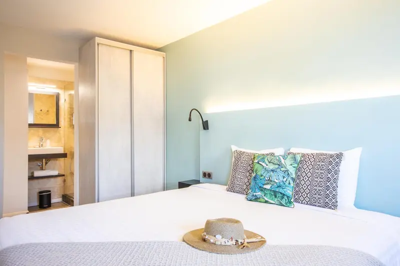Une chambre lumineuse avec un grand lit recouvert d'une courtepointe blanche et de coussins.