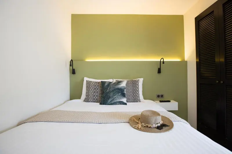 Un lit recouvert d'une couverture blanche et de coussins decoratifs dans une chambre lumineuse.