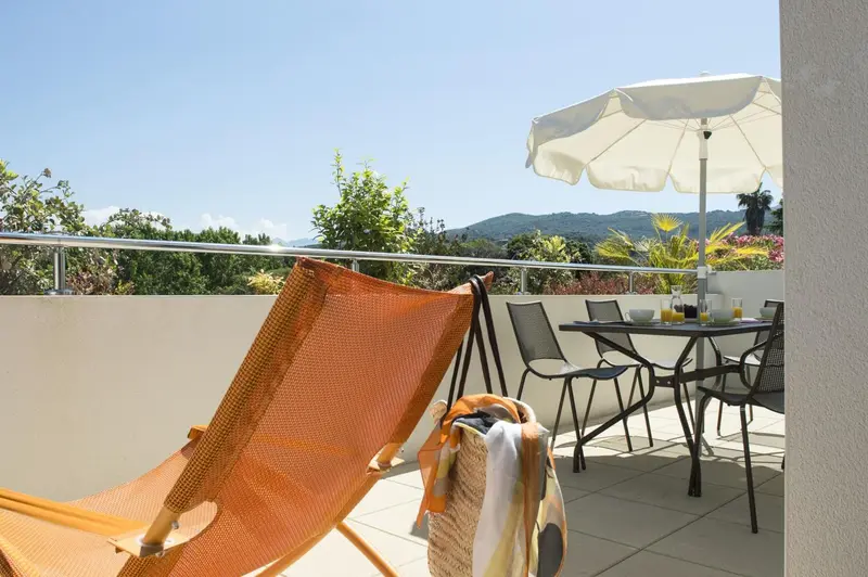 Une terrasse ensoleillée offre une vue sur la végétation et les collines environnantes.