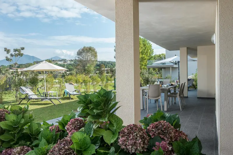 Terrasse ombragée donnant sur un jardin verdoyant et des montagnes.
