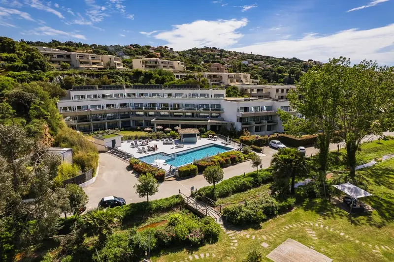 Vue aérienne d'un complexe hôtelier blanc avec une piscine et des espaces verts.