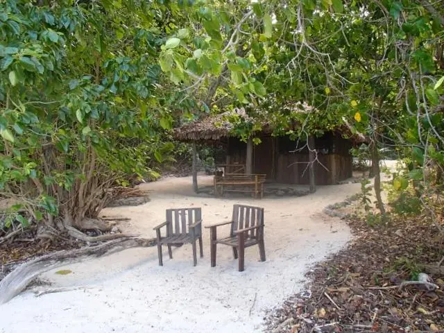 Petite cabane en bois sur une plage de sable blanc, entourée de végétation.