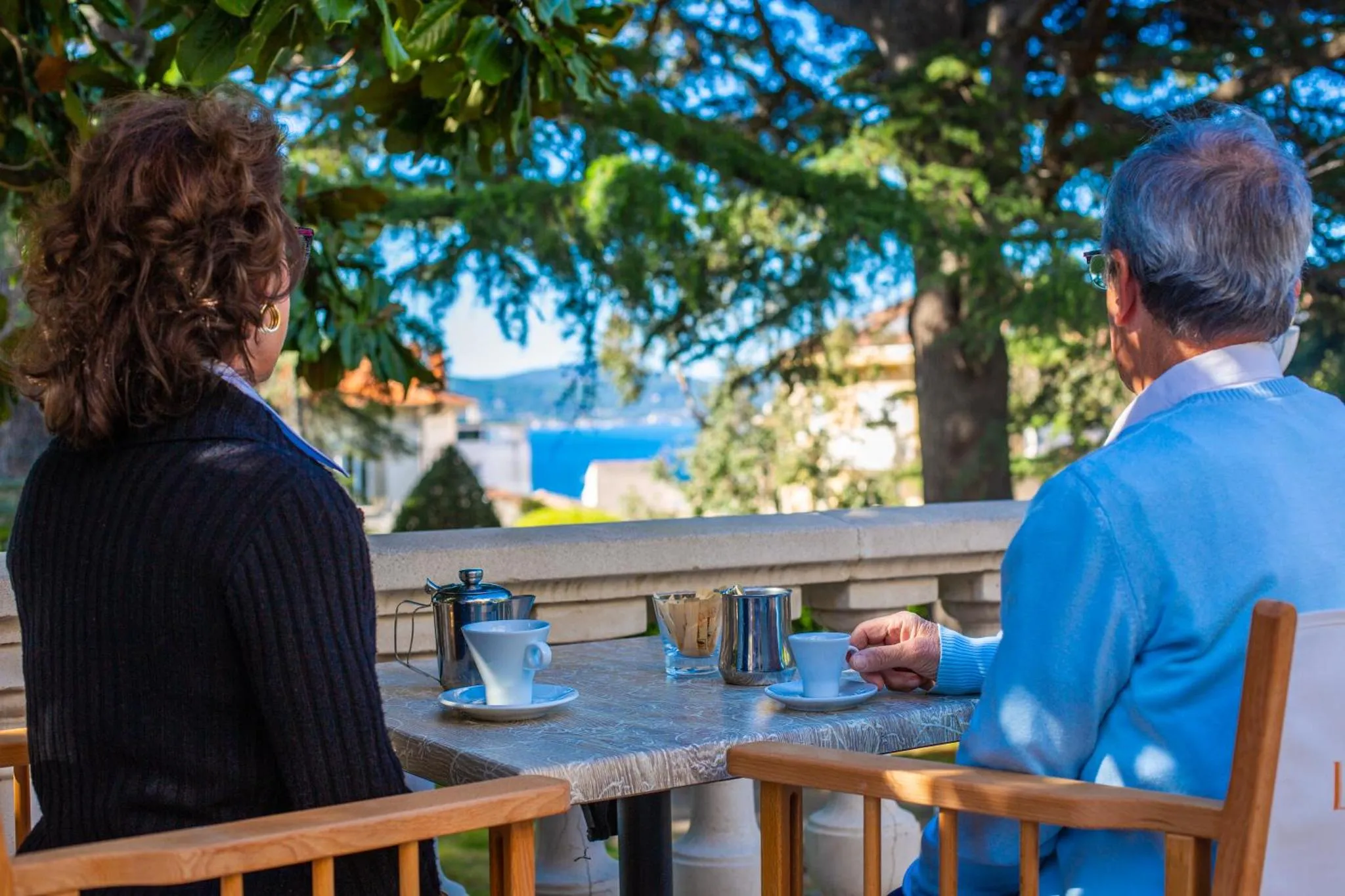 Deux personnes sont assises à une table en extérieur, face à la mer.