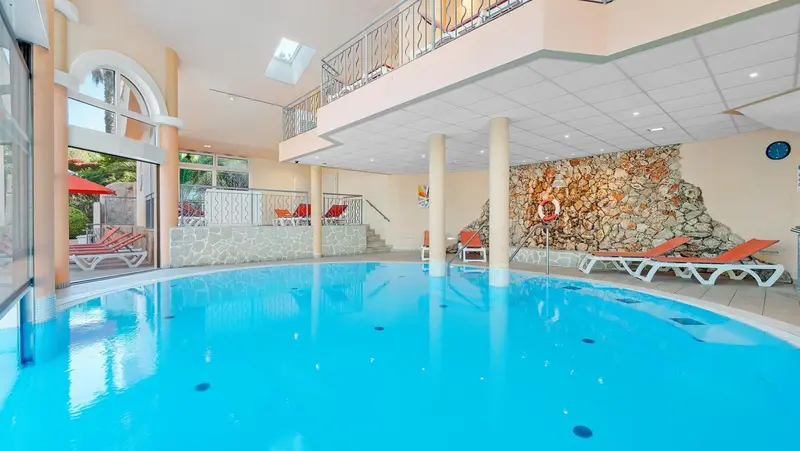 Une piscine intérieure lumineuse avec des transats et une décoration murale en pierre.