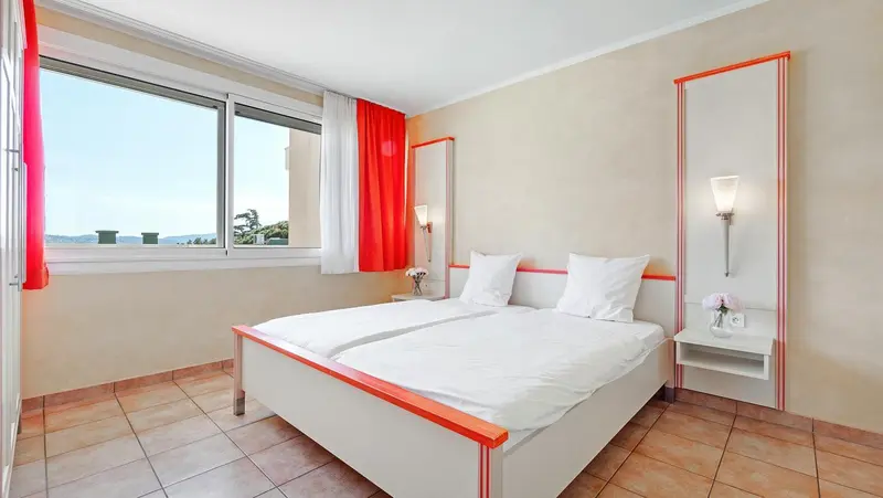 Chambre lumineuse avec deux lits simples et vue sur la mer.