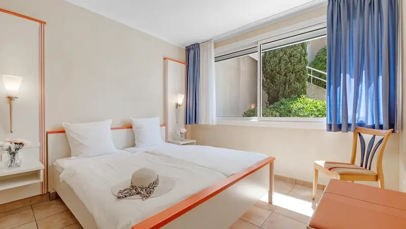 Une chambre lumineuse avec un lit double et une fenêtre donnant sur la végétation.