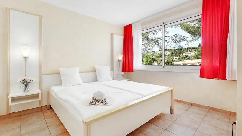Une chambre lumineuse avec un lit blanc et des rideaux rouges.