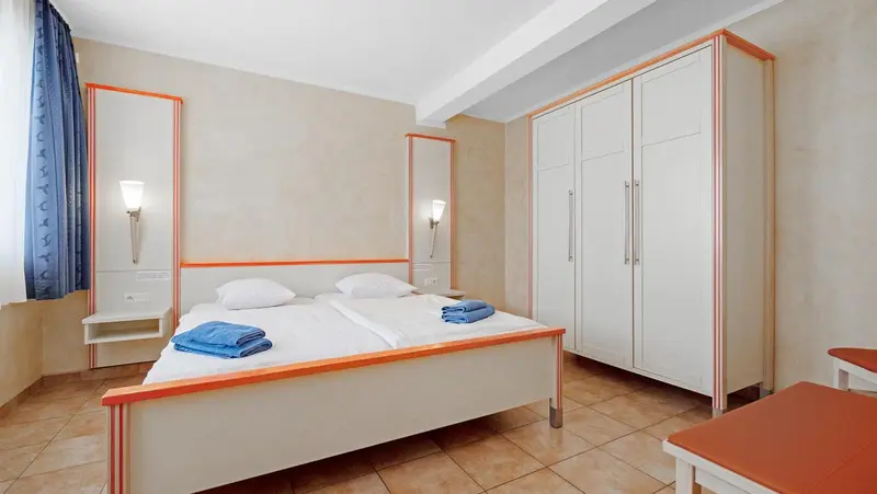 Une chambre lumineuse avec deux lits simples et des armoires blanches.