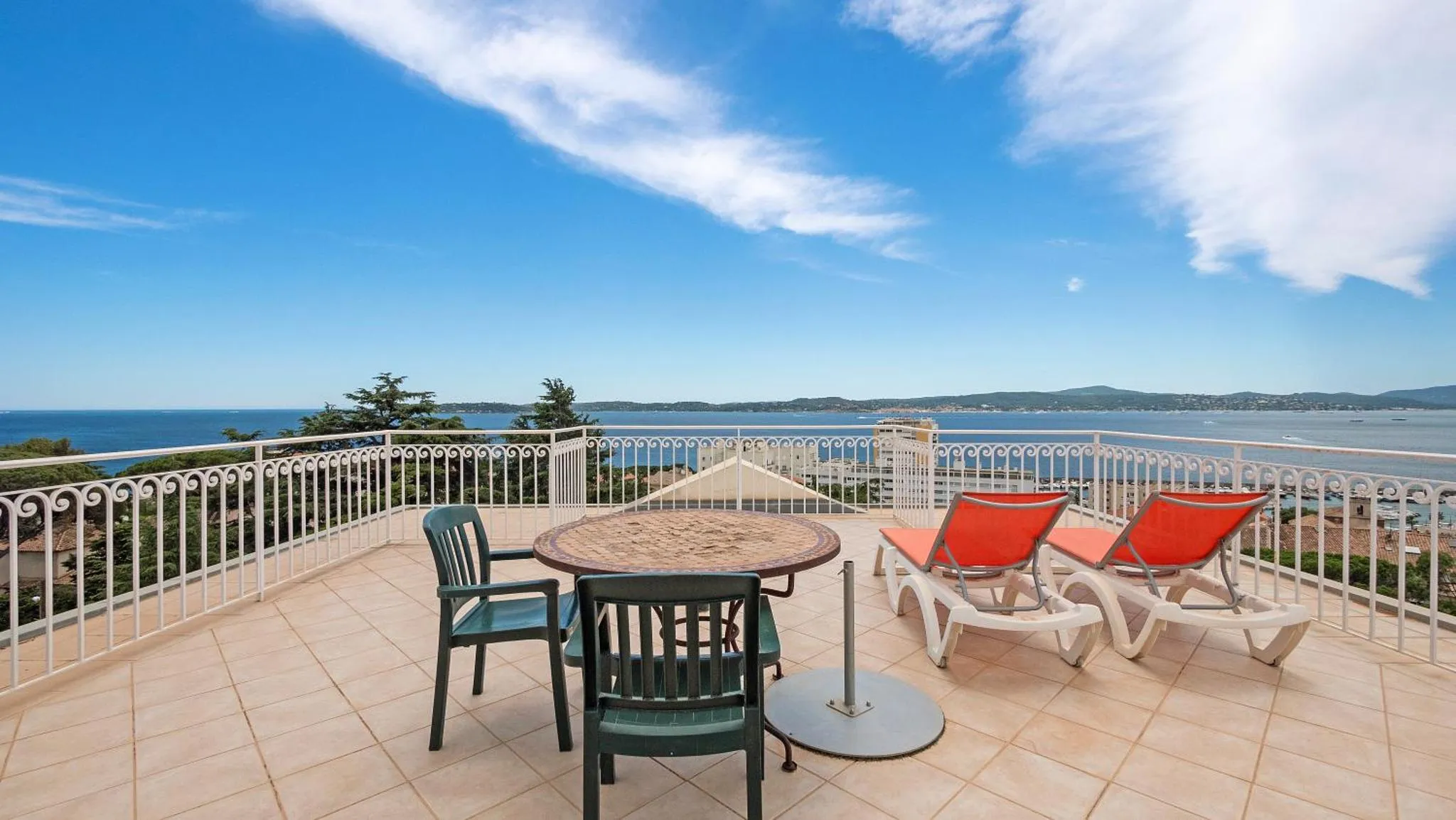 Terrasse carrelée avec mobilier de jardin et vue sur la mer.