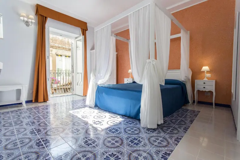 Une chambre lumineuse avec un lit à baldaquin bleu et des carreaux au sol.