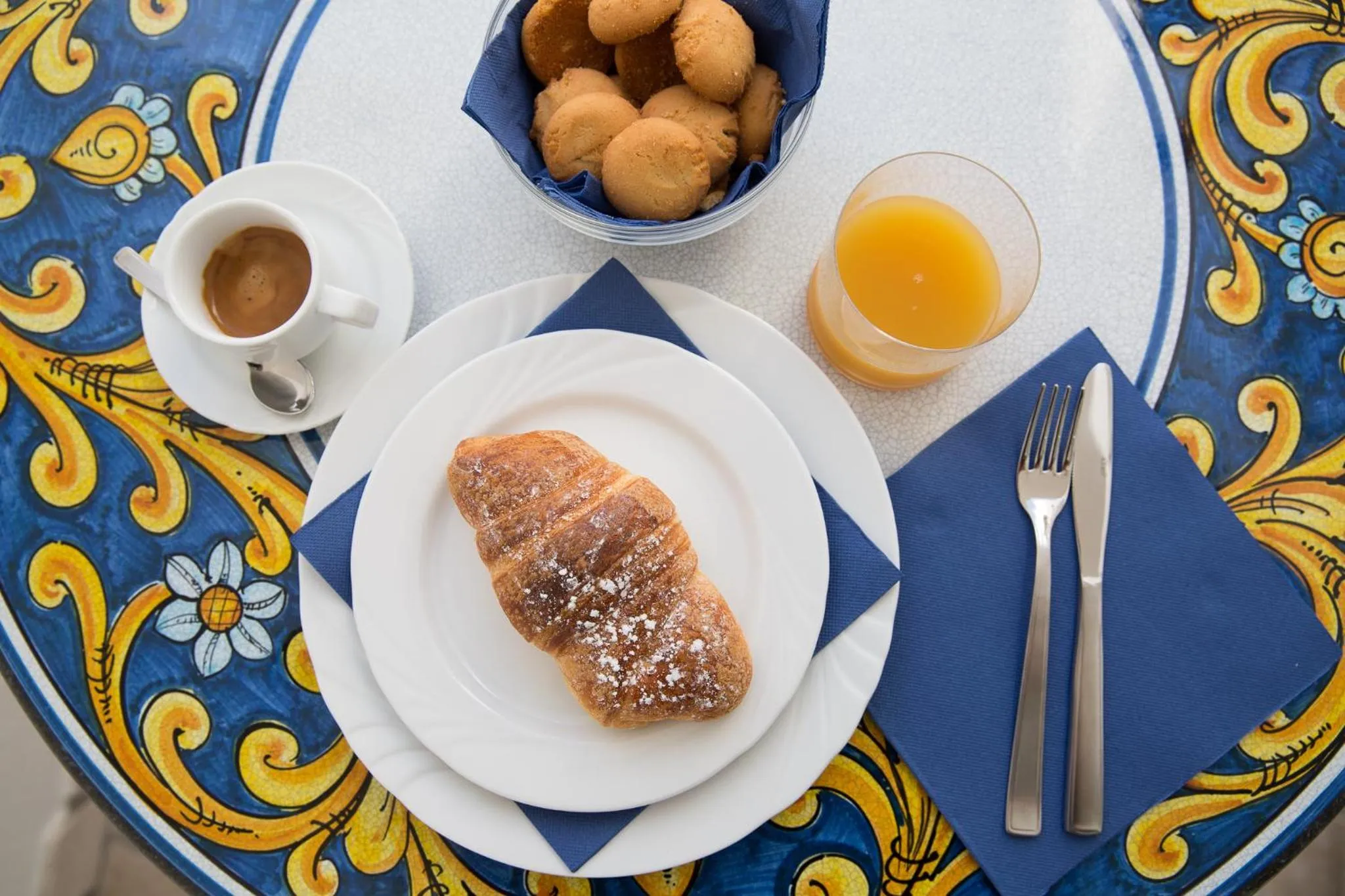 Une table ronde est dressée avec un croissant, une tasse de café et un jus d'orange.
