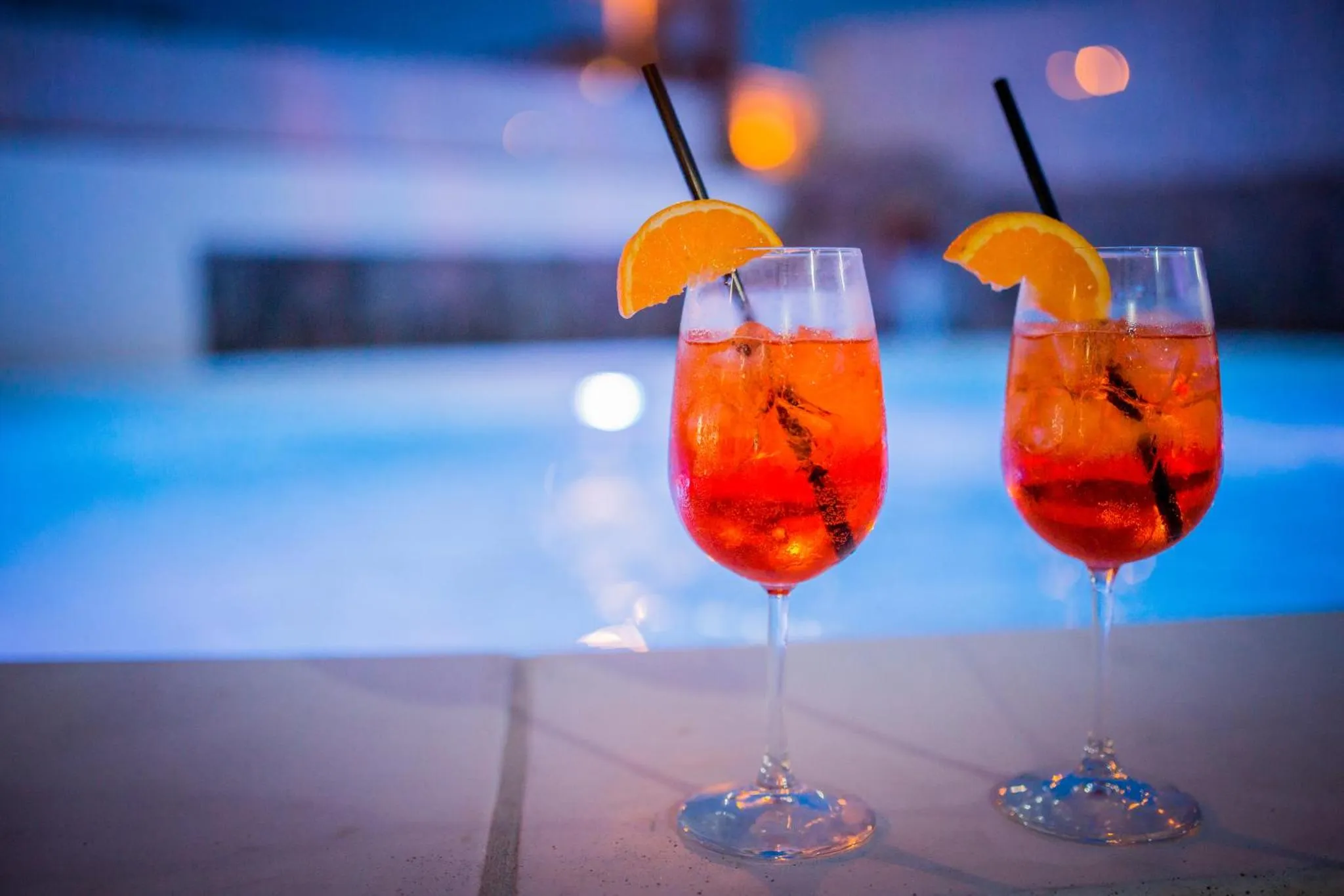 Deux cocktails aux agrumes sont servis au bord d'une piscine illuminée.