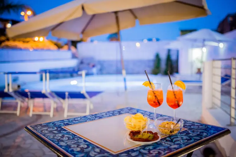 Deux cocktails colorés et des amuse-gueules sont servis sur une table près d'une piscine illuminée.