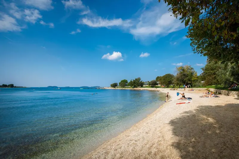 Une plage de galets bordée d'une eau turquoise sous un ciel bleu.