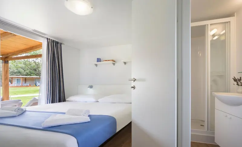 Chambre lumineuse avec un lit fait et une salle de bain attenante.
