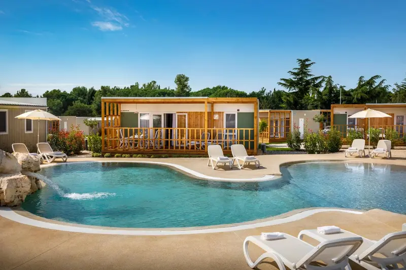 Petite piscine devant des bungalows en bois avec transats.