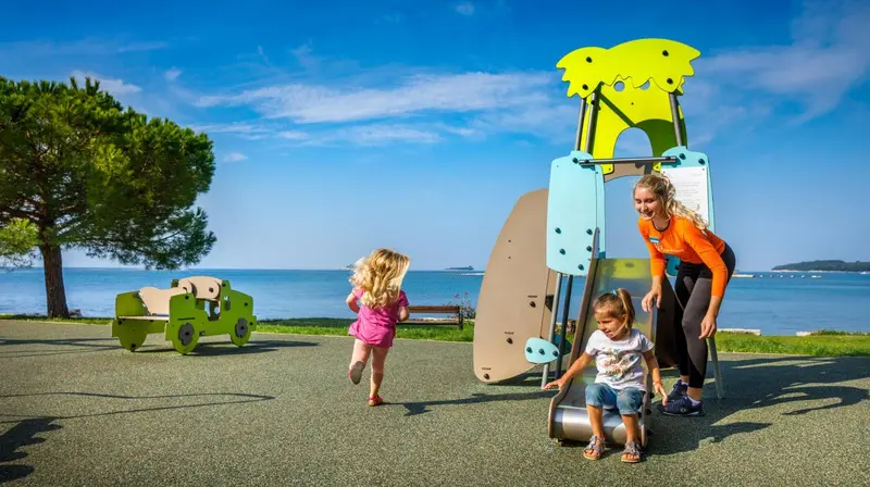 Des enfants jouent sur une aire de jeux en bord de mer ensoleillé.